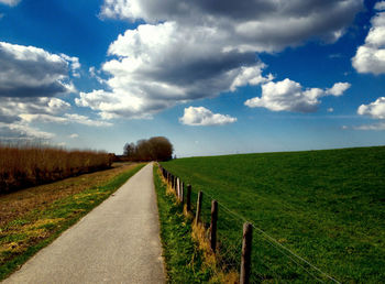 Street by grassy landscape against sky