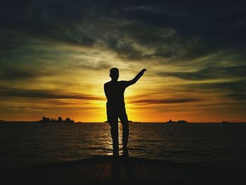 Silhouette man standing by sea against sky during sunset