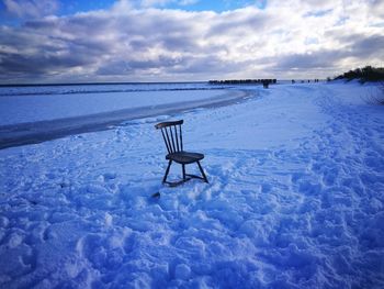 Empty chairs on snow covered land against sky