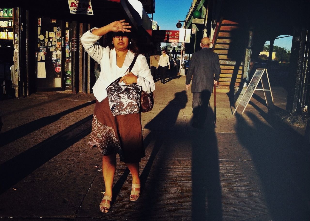 lifestyles, leisure activity, building exterior, casual clothing, young adult, full length, standing, built structure, street, front view, architecture, young women, city life, person, sunglasses, sunlight, city, shadow