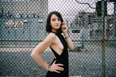 Side view of woman looking away while standing by chainlink fence