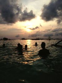 Silhouette people swimming in sea against sky during sunset