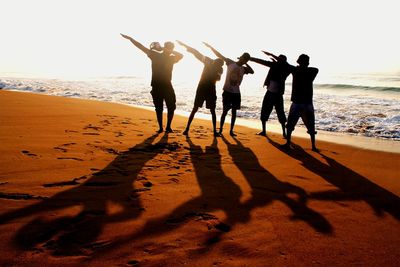 Silhouette people standing on beach against sky during sunset