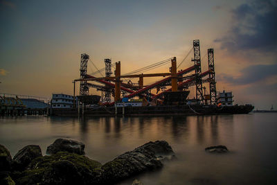 Cranes at pier against sky during sunset