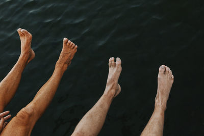 Low section of people sitting at sea barefoot