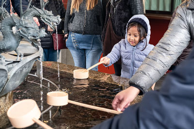 People with ladle by fountain at shrine