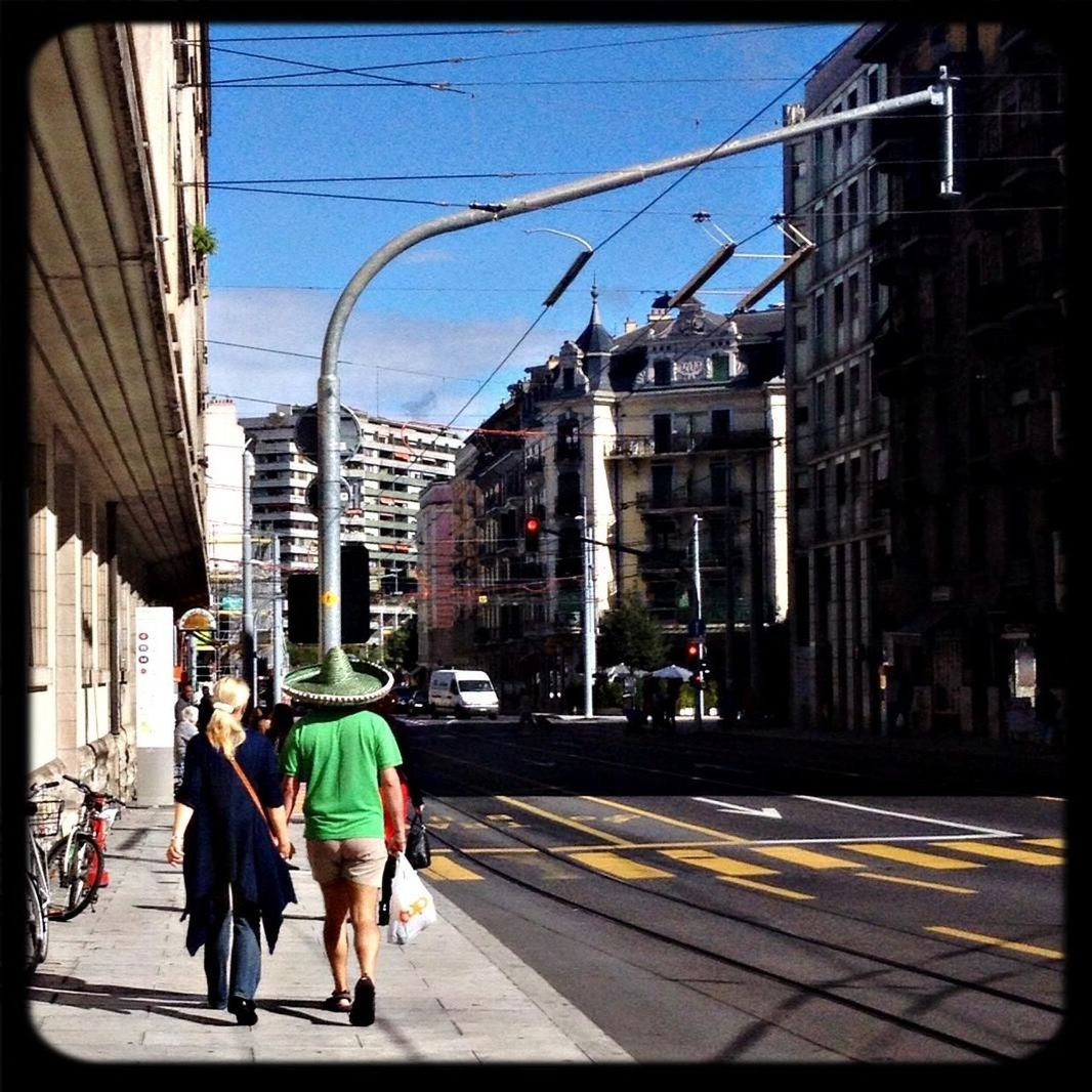 building exterior, architecture, built structure, men, street, city, walking, transfer print, person, city life, rear view, auto post production filter, full length, lifestyles, transportation, sunlight, sidewalk, power line, sky