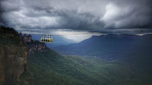 Overhead cable car over mountains against cloudy sky