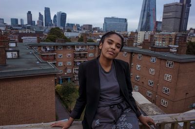 Portrait of smiling young woman in city against sky