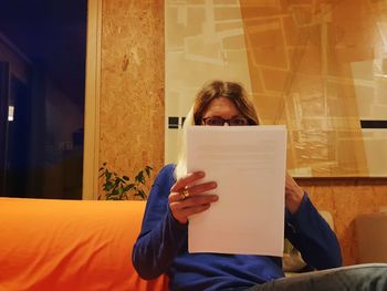 Woman reading papers while sitting on sofa at home