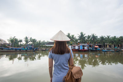 Rear view of woman wearing asian style conical hat standing by lake