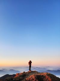 Rear view of man standing on mountain against clear sky during sunset