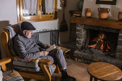 High angle view of man reading book while sitting by fireplace at home
