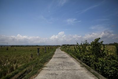 Dirt road amidst field against sky