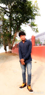 Young man looking away while standing against tree