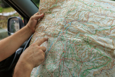 Cropped image of hand pointing at map while sitting in car