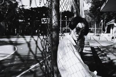 Close-up of lonely young woman sitting by chainlink fence