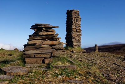 Stack of stones on field against clear blue sky