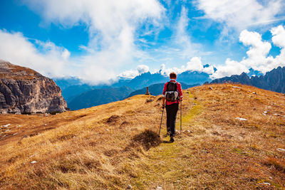 Rear view of hiker walking on mountain against sky