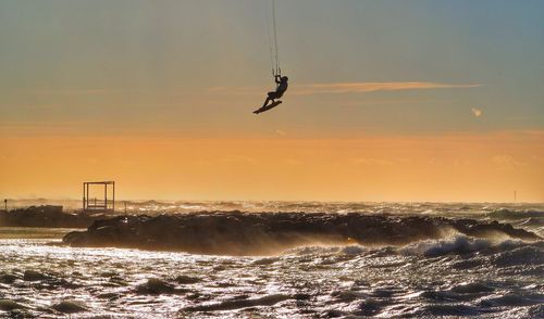 Silhouette man hanging above sea during sunset