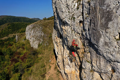 Flying near a mountain rescuer rappelling on a rocky wall with a drone