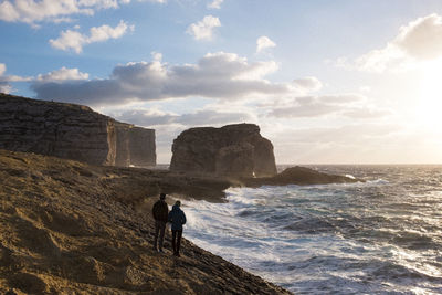 Man standing on cliff by sea against sky