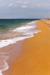 Beautiful calm scene of empty sandy beach, turquoise colored water and cloudy sky. waves crash onto