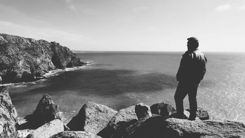 Rear view of woman standing on rock by sea against clear sky