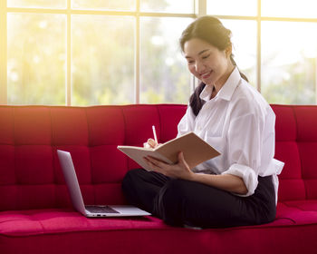 Young woman using phone while sitting on laptop