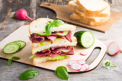 Double sandwich with pastrami and fresh vegetables and herbs on a cutting board. american snack. 