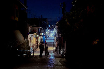 Rear view of silhouette people on street amidst buildings at night