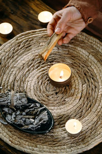 Woman hands burning palo santo, before ritual on the table with candles and green plants. smoke of