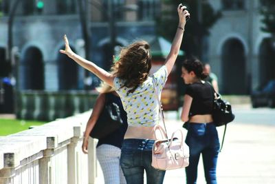 Rear view of excited woman with arms raised walking on footpath