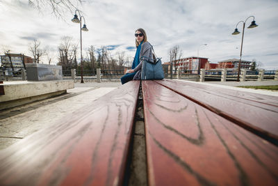 Side view of woman sitting on bench against sky