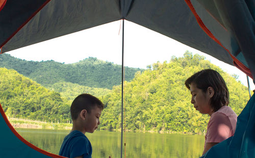 Side view of mother and son seen through tent against lake