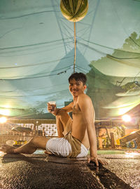 Young man sitting on woman holding umbrella against sky