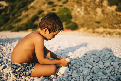 Side view of boy sitting on rock