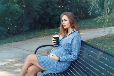 Pregnant young woman sitting on bench in park