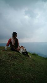 Young woman sitting on field against sky