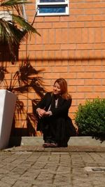 Young woman using mobile phone while standing against brick wall