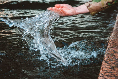 The girl's hand surging water and drops and splashes fly. touching the river with the palm 