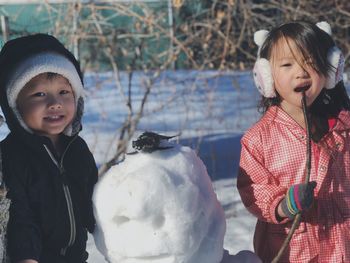 Portrait of cute siblings standing by snow on field