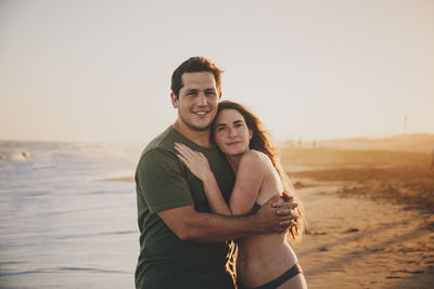 Portrait of young couple standing against sea during sunset