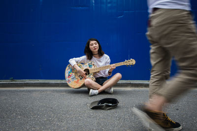 Woman playing guitar against blue wall