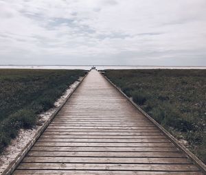 Boardwalk leading towards landscape against sky