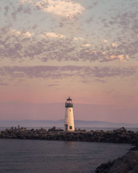 Lighthouse by sea against sky during sunset