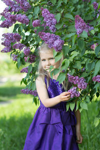 A girl in a lilac dress in a blooming park next to a lilac bush