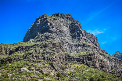 Low angle view of rocky mountain against blue sky