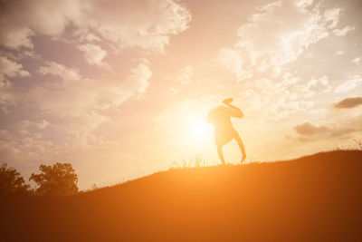 Silhouette woman standing on field against sky during sunset