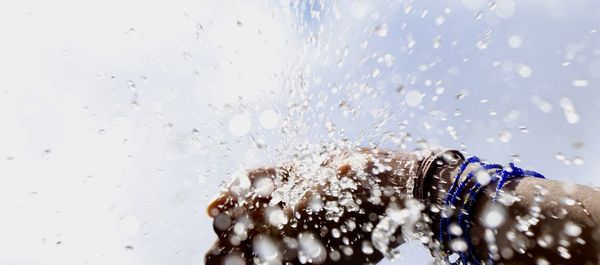 Close-up of woman splashing water against the sky as background 